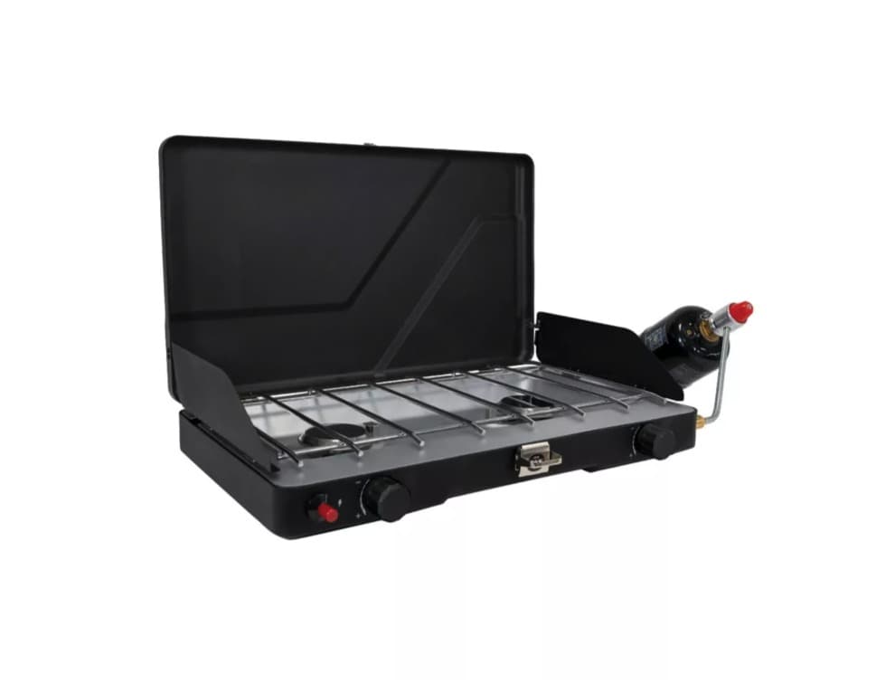 A black Field & Stream two-burner tabletop propane stove with the lid raised and side windscreens up, chrome grate over the burners, and a green one-pound propane cylinder attached to the regulator on the right.
