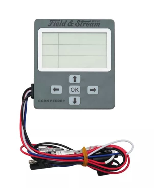A Field & Stream digital game-feeder timer, a grey box with a large blank LCD, four arrow keys and an OK button, with a coiled wiring harness of red, black, blue and white leads below it.