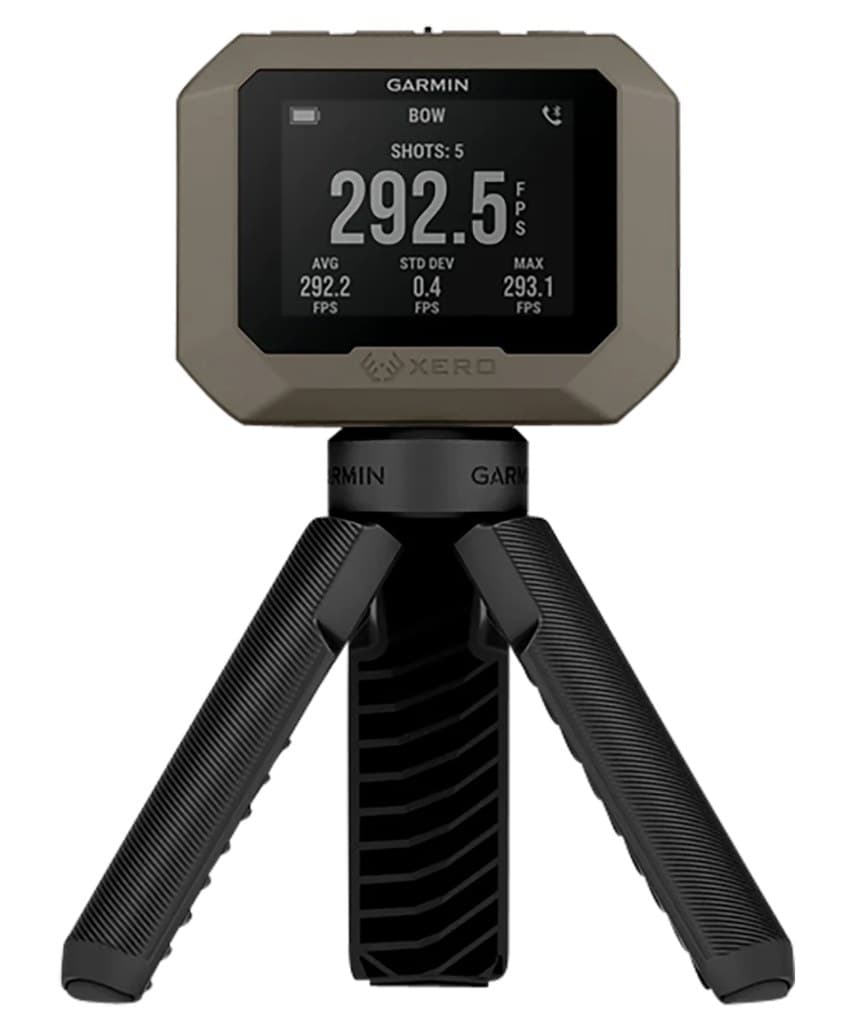 A Garmin Xero C1 Pro chronograph on a small black tripod, seen face on: a tan body around a lit display reading BOW, shots 5, 292.5 FPS, with average, standard deviation and max beneath it.