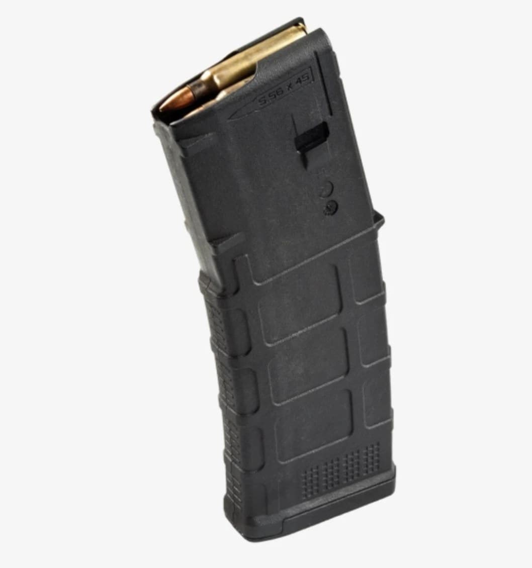 A black Magpul PMAG 30 GEN M3 rifle magazine standing on a light grey backdrop, tilted slightly, three 5.56 rounds showing at the feed lips and 5.56 x 45 moulded into the body.