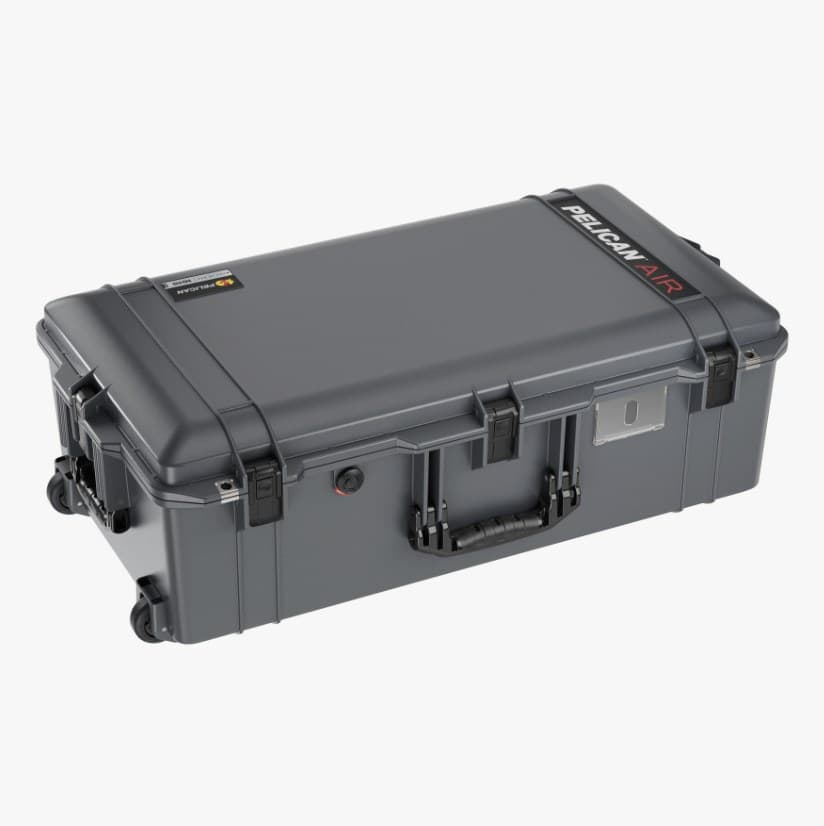 A Pelican 1615 Air case in graphite seen from three-quarters above, lid closed with the PELICAN AIR logo along the top edge, four latches down the front, the trolley handle and two wheels at the left end.