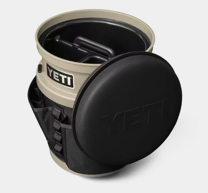 A tan YETI LoadOut bucket with the black swivel seat swung open on top and the black gear belt around the outside, seen from above.