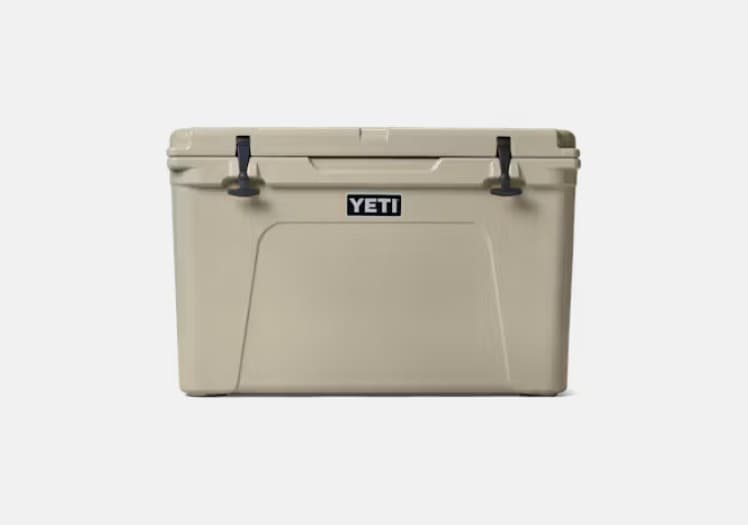 A YETI Tundra 105 hard cooler in tan, seen square from the front, with two black rubber latches on the lid and the YETI badge above a recessed panel.